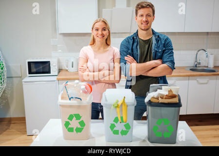 Le tri des déchets à la maison. Protéger l'environnement. Jeune famille heureuse de mettre les déchets dans les poubelles de couleur verte avec l'icône de recyclage dans la cuisine Banque D'Images