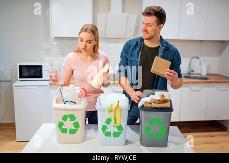 Le tri des déchets à la maison. Smiling young family plaçant le plastique, papier, d'autres déchets dans des poubelles dans la cuisine bio Banque D'Images