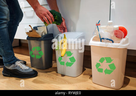 Le tri des déchets à la maison. Portrait de l'homme mettre le brocoli dans la poubelle. Poubelles colorées pour le tri des déchets dans la cuisine Banque D'Images