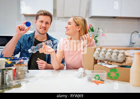 Le recyclage. Conscient jeune famille le tri des bouteilles en plastique vides et les couvercles en étant assis à la table avec d'autres déchets à la maison Banque D'Images