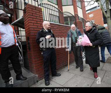 Un agent de police se tient à l'extérieur de la mosquée de Finsbury Park à Londres, que les résidants locaux, Paul et Barbara Smith, arriver à laisser les fleurs, à la suite de l'attaque de la mosquée de Christchurch en Nouvelle-Zélande. Banque D'Images