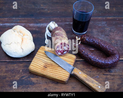 Saucisses de porc ibérique sur une vieille planche en bois avec un morceau de fromage de brebis, un ancien couteau et un verre de vin rouge Banque D'Images