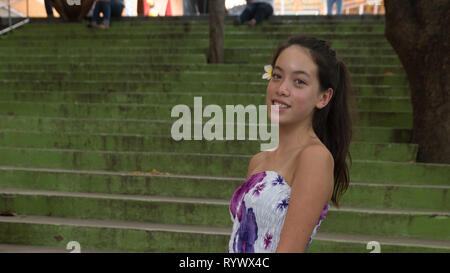 Smiling young girl standing in front of green escaliers avec une fleur dans ses cheveux Banque D'Images