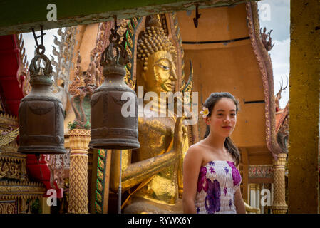 Teenage Girl standing barefoot en face de la rangée de cloches au temple bouddhiste Banque D'Images