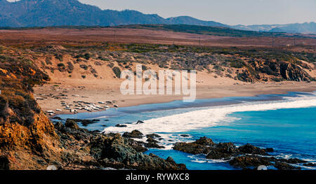 Donnant sur cove avec des roches et le bleu océan avec des vagues se brisant sur la côte de sable. Banque D'Images