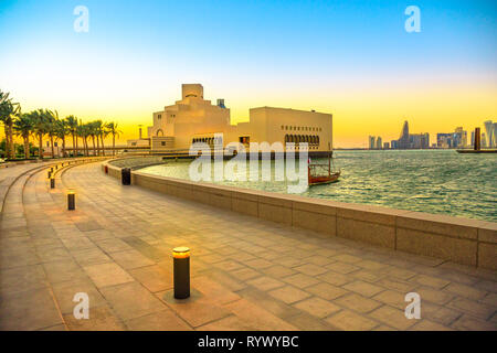 Promenade en bord de mer avec des palmiers le long de la baie de Doha et gratte-ciel du boutre avec Doha West Bay skyline at sunset. Paysage urbain. Dans la capitale du Qatar Banque D'Images