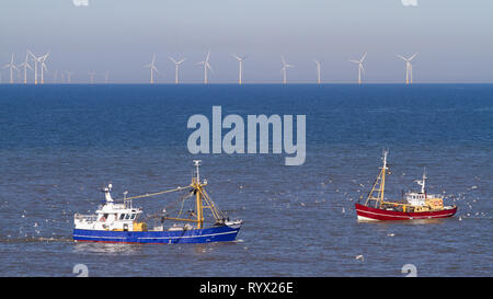 Un bleu et un cutter rouge avec un troupeau de mouettes sur la mer du Nord, au soleil, avec des générateurs du vent à l'arrière-plan Banque D'Images