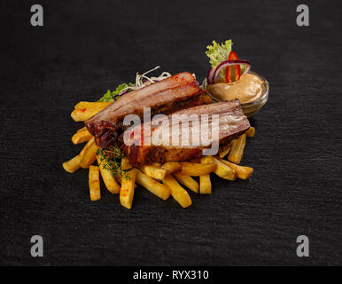 Côtes levées de porc barbecue et frites sur fond d'ardoise noire Banque D'Images