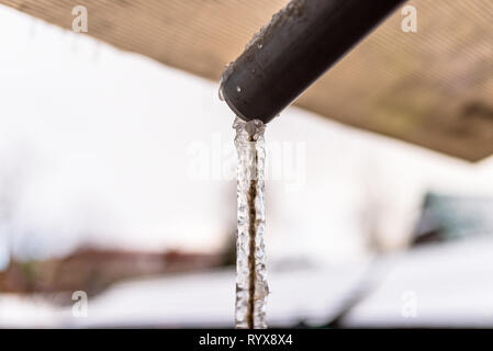 L'eau congelée découlant de la toiture par l'intermédiaire d'un tuyau en plastique avec une chaîne à l'intérieur. Banque D'Images