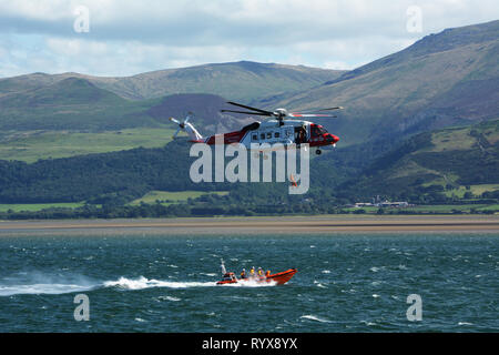 HM Coastguard hélicoptère et pratique de sauvetage Beaumaris transfert d'une personne sauvée sur le détroit de Menai avec montagnes de Snowdonia en arrière-plan Banque D'Images