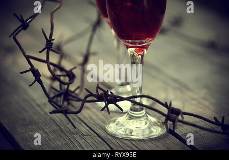 Barbelés rouillés et verres de vin rouge sur une table. La dépendance alcoolique. Banque D'Images