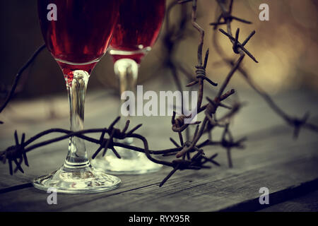 Lunettes avec boisson alcoolisée et un fil de fer barbelé rouillé sur une table en bois. La dépendance alcoolique. Banque D'Images