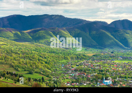 Paysages montagneux au printemps. Village de la vallée, crête de montagne avec des taches de neige. beau temps avec ciel nuageux. vue depuis la colline. Banque D'Images