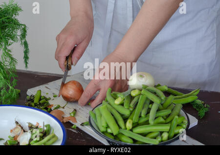 .Femme est hacher des oignons pour la cuisson sur la table..Il y a des fèves fraîches et l'oignon sur la table. Banque D'Images