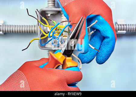 Électricien dans gants de protection est coupant le fil se termine avec l'aide de pinces à bec long. Banque D'Images