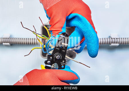 Travailleur dans gants de protection est retirée de l'isolation du câblage en cuivre avec l'aide de cutter pince à dénuder, close-up. Banque D'Images