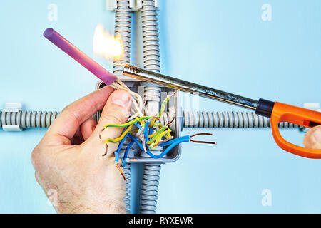 Électricien est en train de mettre le feu le tube thermorétractable pour isolement fils torsadés de boîte de jonction. Banque D'Images