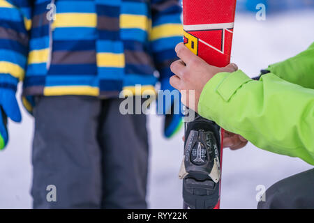 Szklarska Poreba, Pologne - Février 2019 : moniteur de ski holding skis petit garçon et lui expliquant les caractéristiques de sécurité de l'équipement Banque D'Images