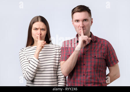 Jeune couple montrant un signe de silence mise en doigt geste bouche sur fond blanc Banque D'Images