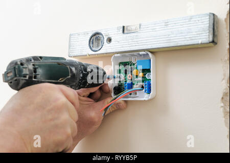 L'installation d'un thermostat programmable. Man's hands fixer l'appareil au mur à l'aide d'un tournevis et d'un niveau à bulle. Banque D'Images