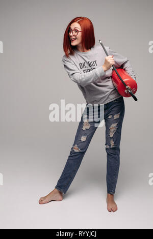 Une femme aux cheveux rouges dans le studio la tenue d'un extincteur. Une femme lumineuse émotionnelle tout éteint avec un extincteur. Banque D'Images