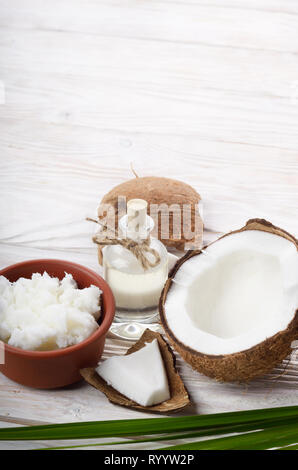 Arrière-plan de la noix de coco, noix de coco, l'huile dans un bol d'argile et de verre sur une table en bois blanc Banque D'Images