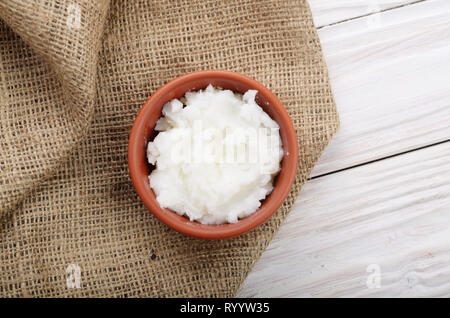 Mise à plat de l'huile de noix de coco dans un bol d'argile brun sur le chanvre sacs sur une table de cuisine en bois blanc Banque D'Images