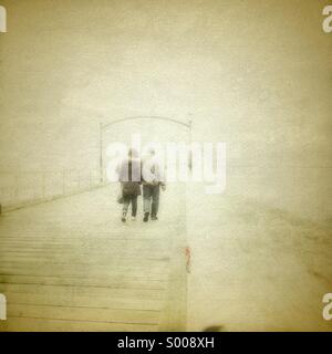 Couple holding hands and walking away le long de la jetée en bord de mer dans le brouillard. Banque D'Images