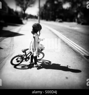 Jeune fille avec son vélo et un panier de fleurs. Ombre et soleil fort Banque D'Images