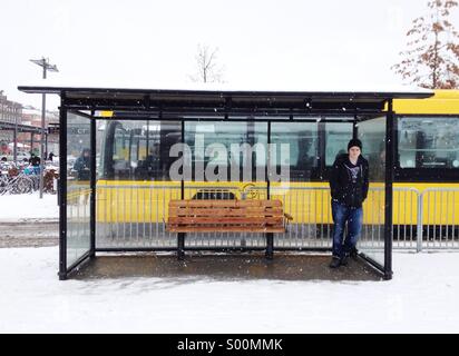 Jeune homme est en attente de bus dans la neige humide en Suède. Banque D'Images