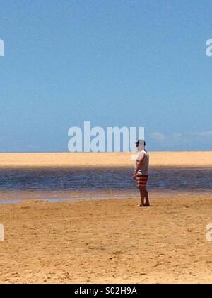 Homme avec short et teeshirt et cap sur la plage de l'océan des eaux intérieures par Lake looking out to sea Banque D'Images