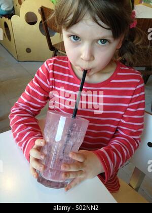 Little girl drinking milk-shake de fruits avec une paille Banque D'Images