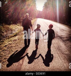 Une mère marche main dans la main avec ses enfants dans le soleil du printemps... Banque D'Images