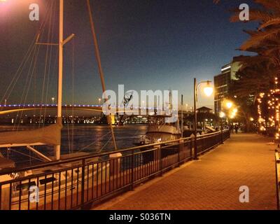 Un début de soirée le long de la rivière St John's dans le centre-ville de Jacksonville, Floride, USA, avec un voilier et les ponts sur l'eau et des marcheurs dans la distance Banque D'Images