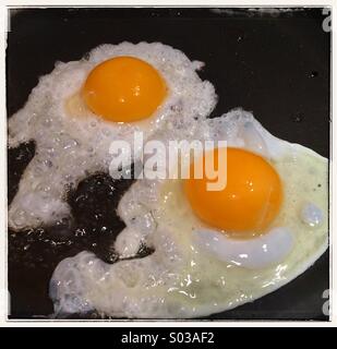 Deux oeufs de poules frais d'être frit dans une poêle pour un petit-déjeuner anglais traditionnel Banque D'Images