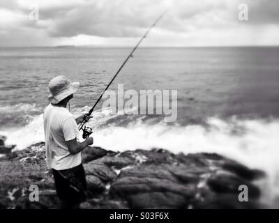 Image en noir et blanc avec point sélectives de pêche pêcheur de surf d'une saillie rocheuse Banque D'Images
