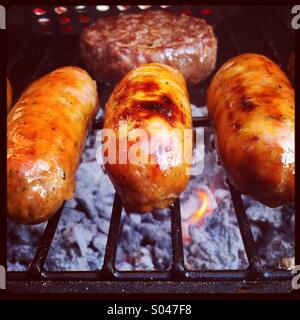 Trois saucisses et d'un hamburger cuisson sur un barbecue Banque D'Images