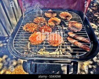 Bacon wrapped hotdogs et hamburgers sur un barbecue Banque D'Images