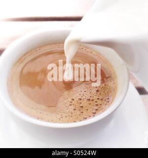 Le lait est versé dans tasse de café Banque D'Images