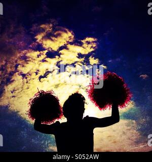 Cheerleader pompons ondulant contre ciel dramatique Banque D'Images