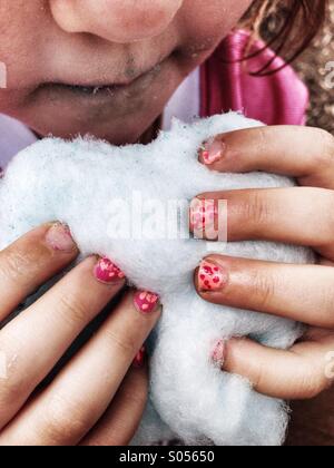 Petite fille mange de la barbe à papa avec des mains sales et peint les ongles. Banque D'Images