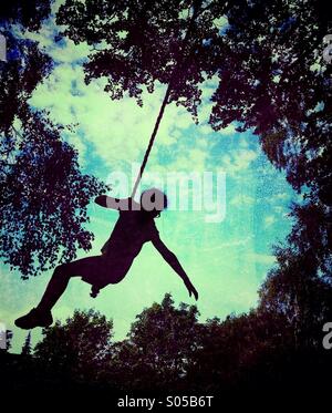 Fille sur rope swing en silhouette contre le ciel Banque D'Images