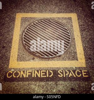 L'espace confiné au pochoir sur le sol sous un carré jaune et couvercle de vidange Banque D'Images