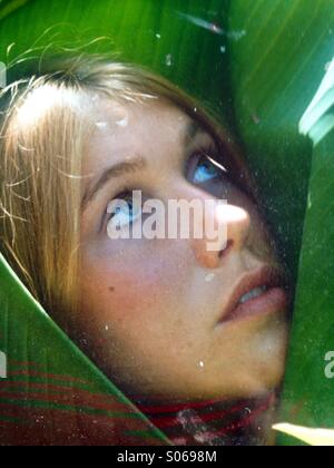 Young woman's face verticale vers le haut à enveloppé dans une feuille de banane verte correspondant à ses yeux. Banque D'Images