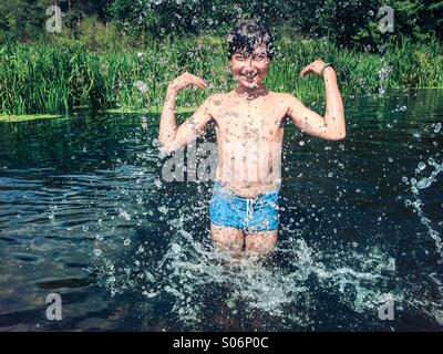 Jeune garçon de s'éclabousser dans la rivière. À l'arrière-plan vert Banque D'Images