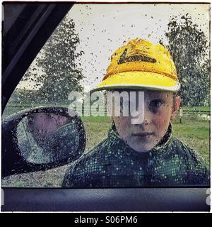 Portrait garçon à travers la fenêtre d'une voiture dans un matin pluvieux. Banque D'Images