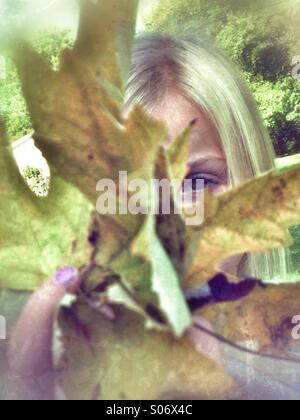 Un enfant peeking through feuilles. Banque D'Images