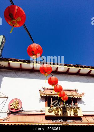 Lanternes chinoises rouge suspendu au-dessus de la rue dans le quartier chinois en face d'une boutique de souvenirs. Banque D'Images
