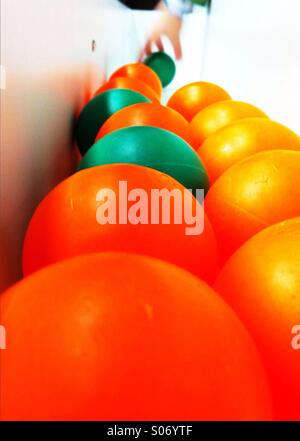 Boules orange et vert et la main d'un enfant d'attraper un ballon vert Banque D'Images