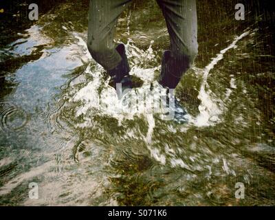 Enfant Splashing in stream dans la pluie Banque D'Images